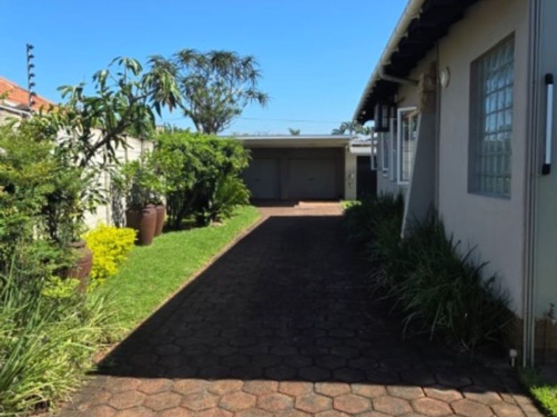 A paved driveway leading to a garage, featuring a side building elevation with a glass block window and perimeter electric fencing.