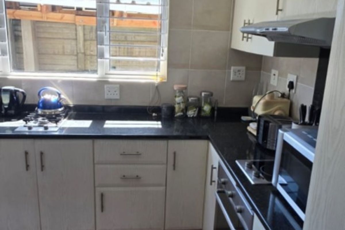 A functional kitchen featuring light-toned cabinetry, dark granite countertops, built-in oven and hob, tiled splashback, and warm timber flooring.