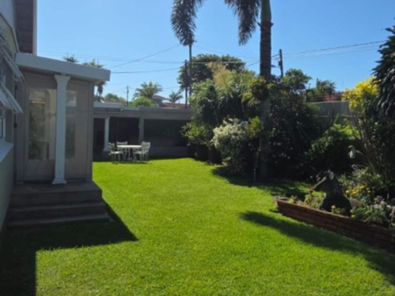 A well-maintained rear garden featuring a lush green lawn, paved patio area, and a covered patio space with mature landscaping.