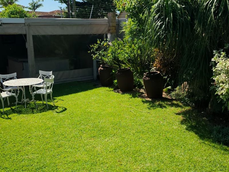 A well-maintained private garden featuring a lush green lawn, mature landscaping, and a covered patio area with electric fencing along the perimeter.