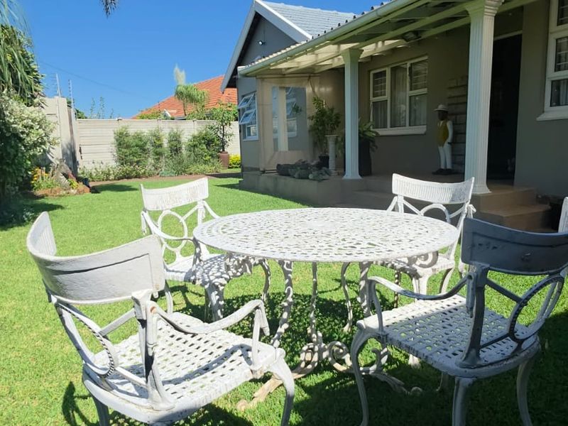A well-maintained rear garden featuring a covered patio area with concrete columns, overlooking a neat lawn and secure boundary wall.