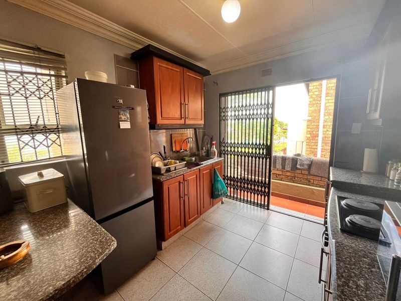 A functional kitchen featuring wooden cabinetry, granite countertops, and direct access to an outdoor balcony area through a security gate.