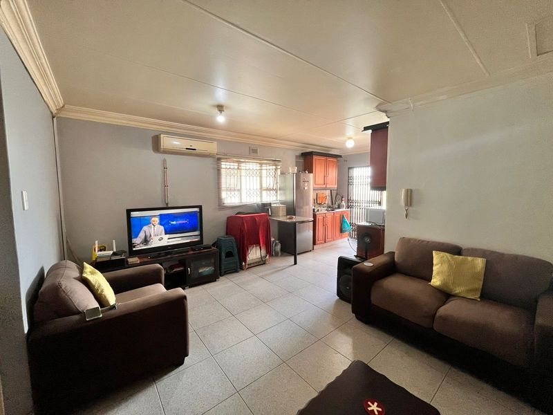 Open-plan living area featuring tiled flooring, a split-system air conditioner, and an adjoining kitchen with wooden cabinetry.