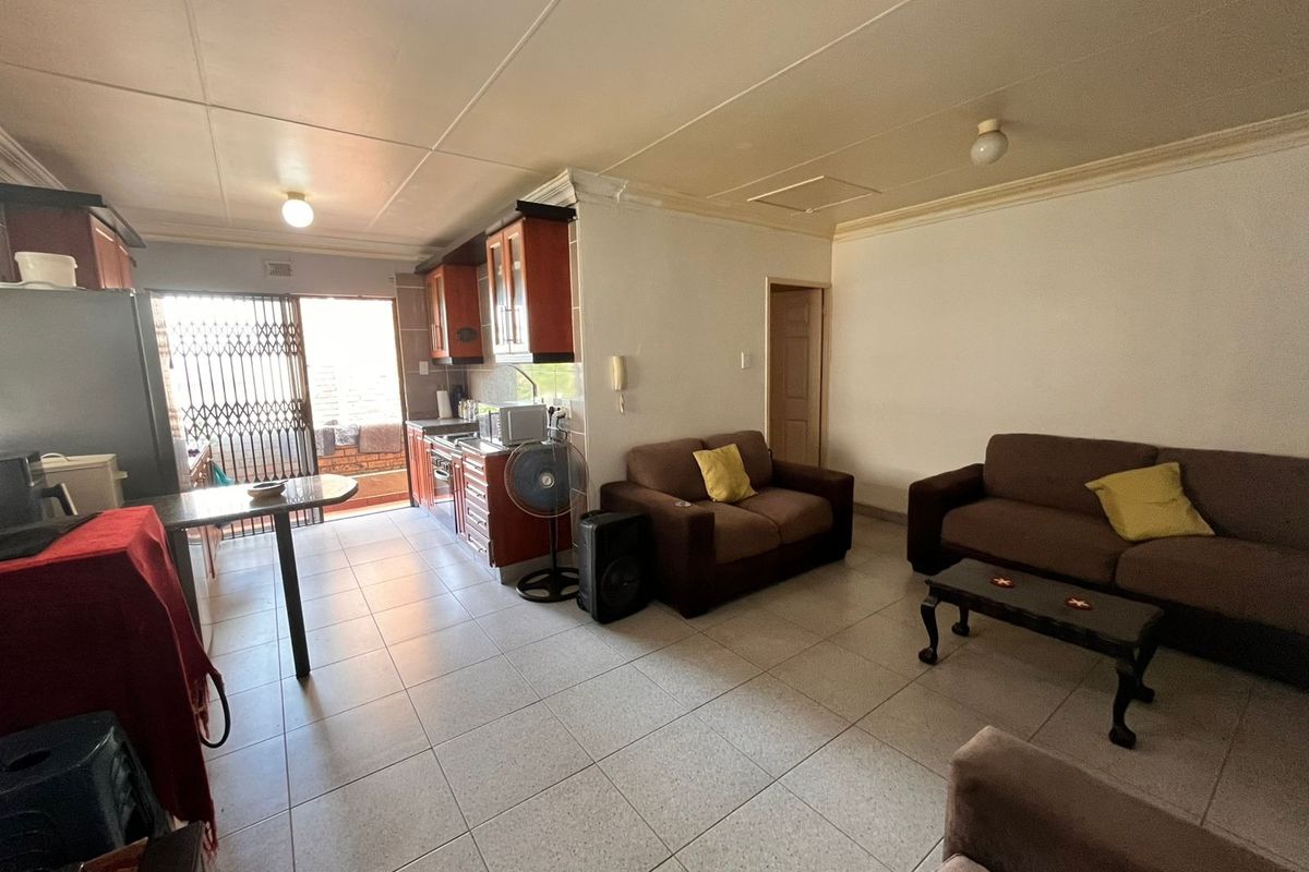 Open-plan living and kitchen area featuring tiled flooring, built-in cabinetry, and direct access to an outdoor space through a security gate.