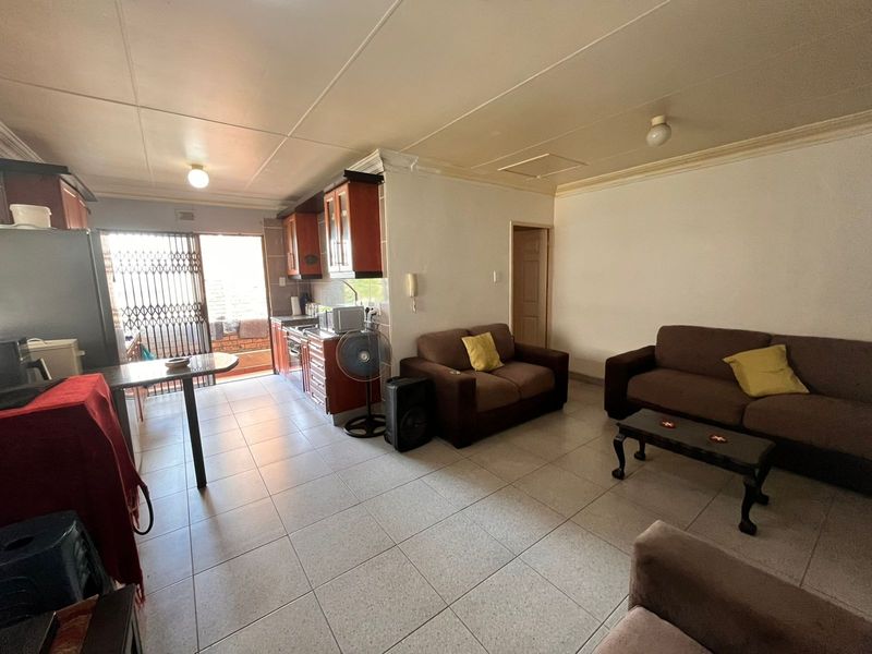Open-plan living and kitchen area featuring tiled flooring, built-in cabinetry, and direct access to an outdoor space through a security gate.
