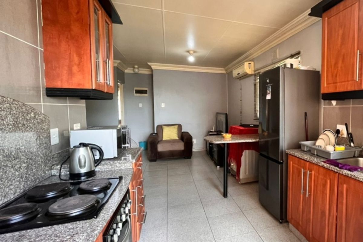Open-plan kitchen and living area featuring granite countertops, wooden cabinetry, electric hob, oven, and tiled flooring throughout.