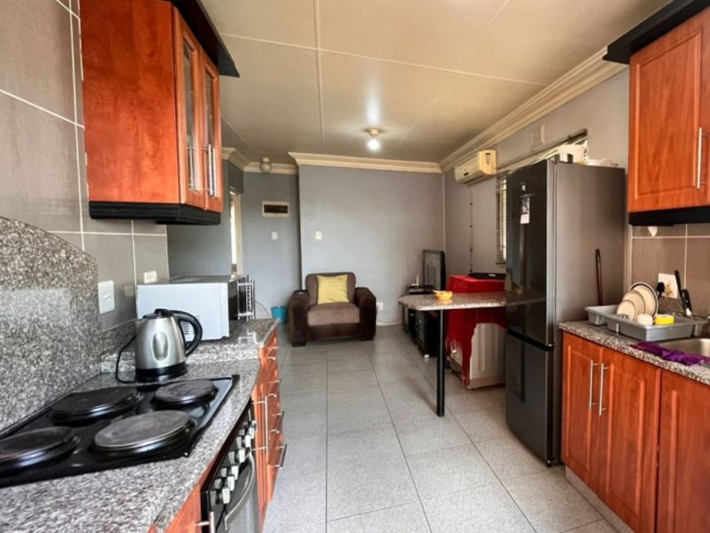 Open-plan kitchen and living area featuring granite countertops, wooden cabinetry, electric hob, oven, and tiled flooring throughout.