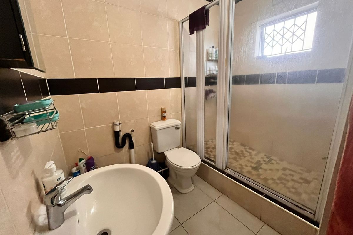 A functional bathroom featuring a shower enclosure, pedestal basin, and toilet with neutral wall tiling and a security-grille window.