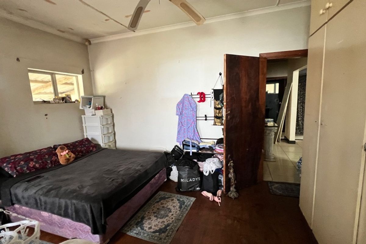 A bedroom featuring timber flooring, built-in cupboards, and a ceiling fan, requiring cosmetic updates to the walls and ceiling.