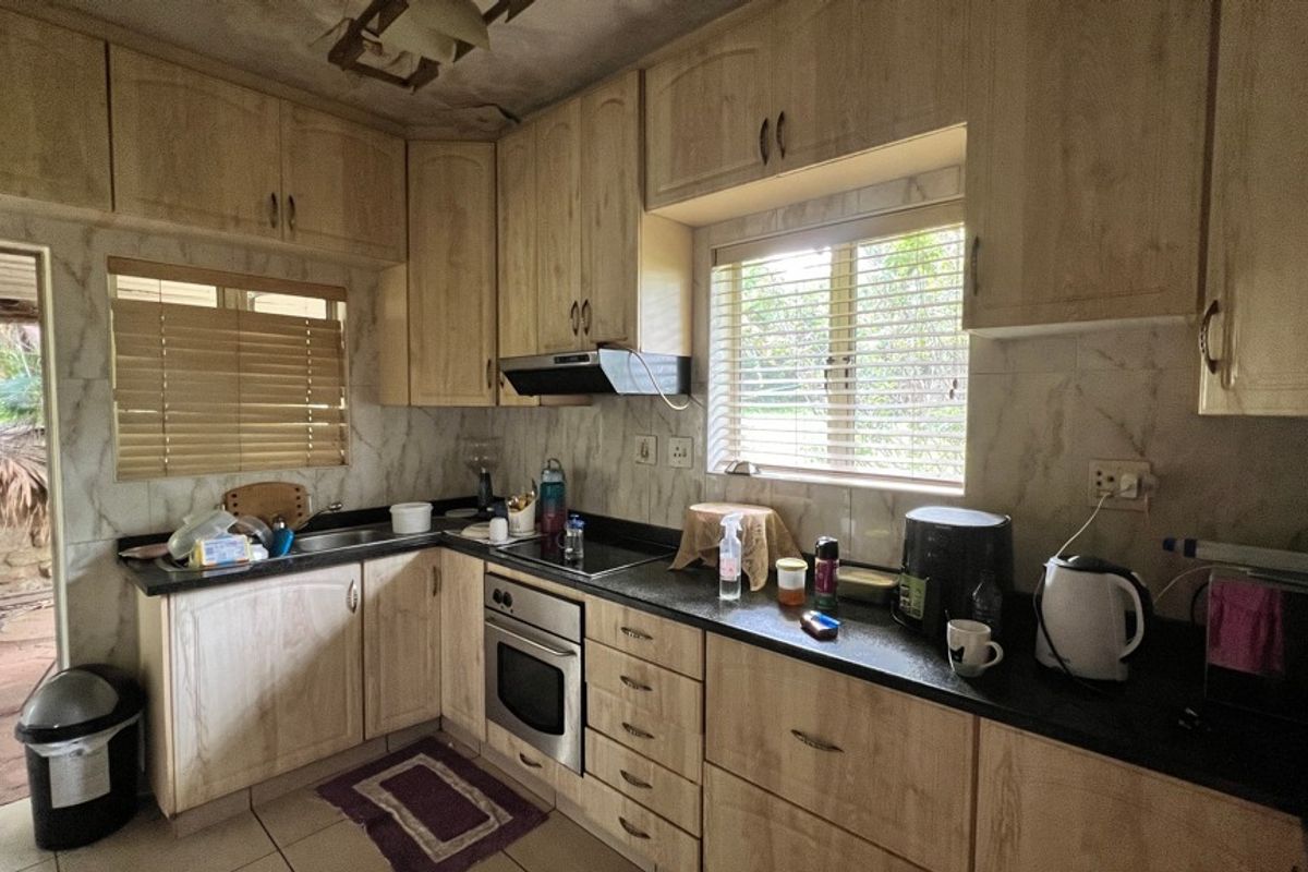 A functional kitchen featuring light wood-tone cabinetry, dark laminate countertops, built-in oven, and hob, with a tiled backsplash and direct access to the exterior.