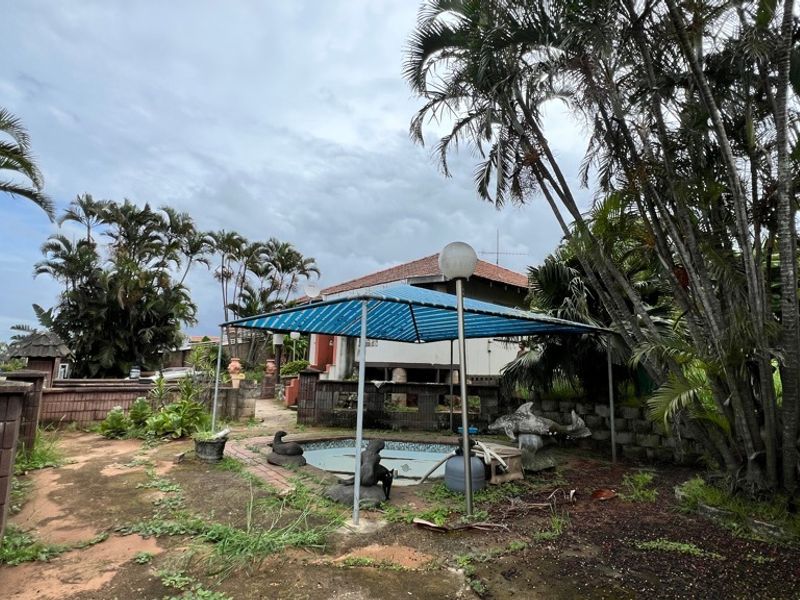 Outdoor pool area featuring a small swimming pool, paved surround, and brick boundary walls, requiring significant landscaping and maintenance to restore.