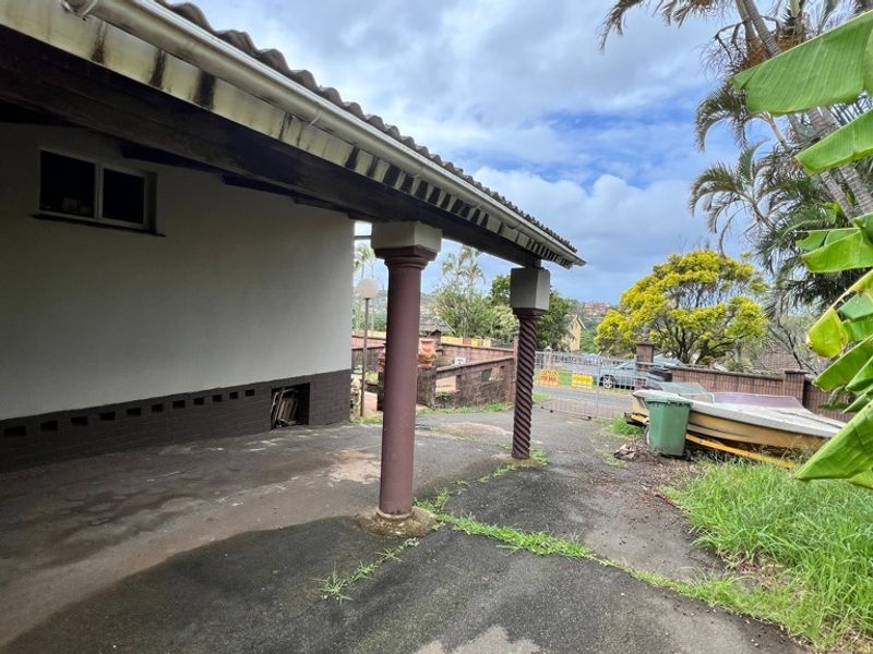A covered outdoor patio area featuring concrete columns and paved flooring, requiring maintenance and landscaping to improve its overall appeal.