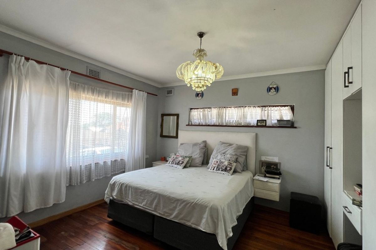 A well-maintained bedroom featuring polished hardwood flooring, built-in wardrobe storage, and a decorative central light fixture.