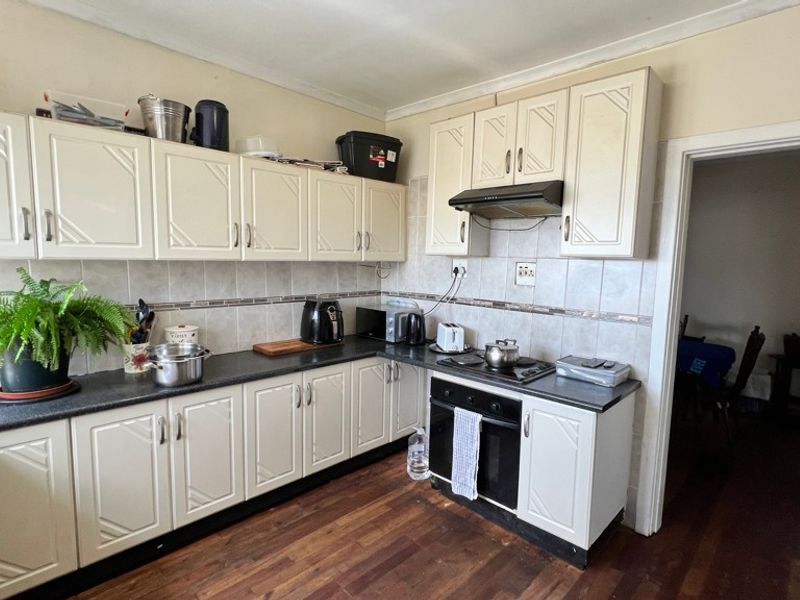 A functional kitchen featuring white cabinetry, dark laminate countertops, tiled backsplash, and integrated cooking appliances with timber flooring.