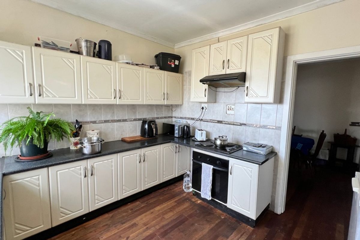 A functional kitchen featuring white cabinetry, dark laminate countertops, tiled backsplash, and integrated cooking appliances with timber flooring.