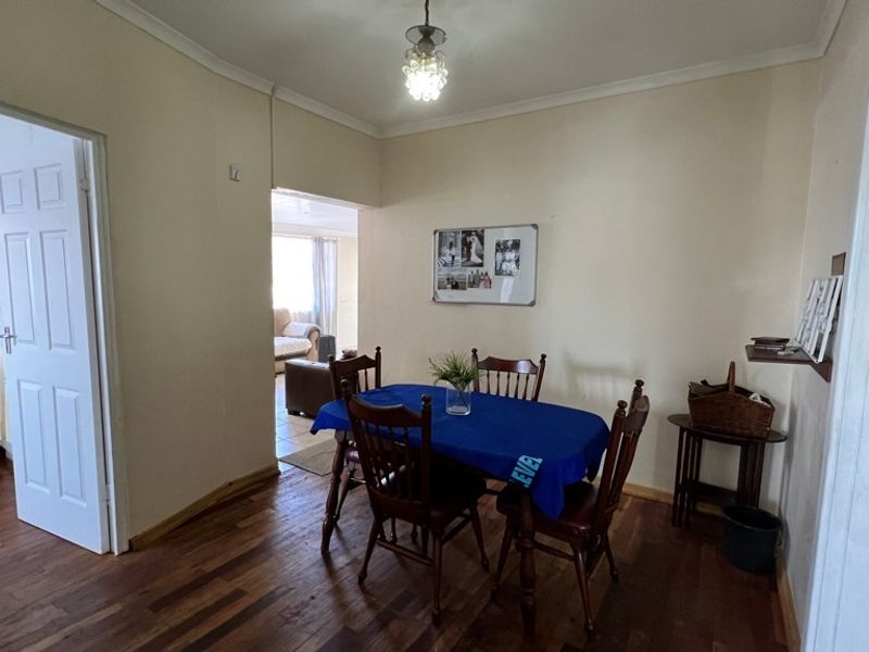 Dining room featuring hardwood flooring, cove cornicing, and a central pendant light fixture, with an open-plan flow into the adjacent living area.