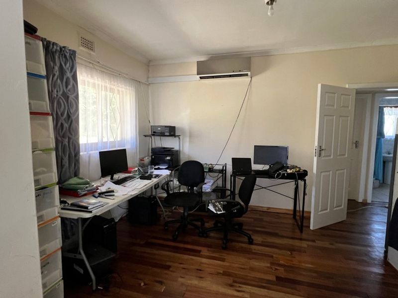 A functional home office space featuring polished hardwood flooring, a wall-mounted air conditioning unit, and built-in storage cabinetry.