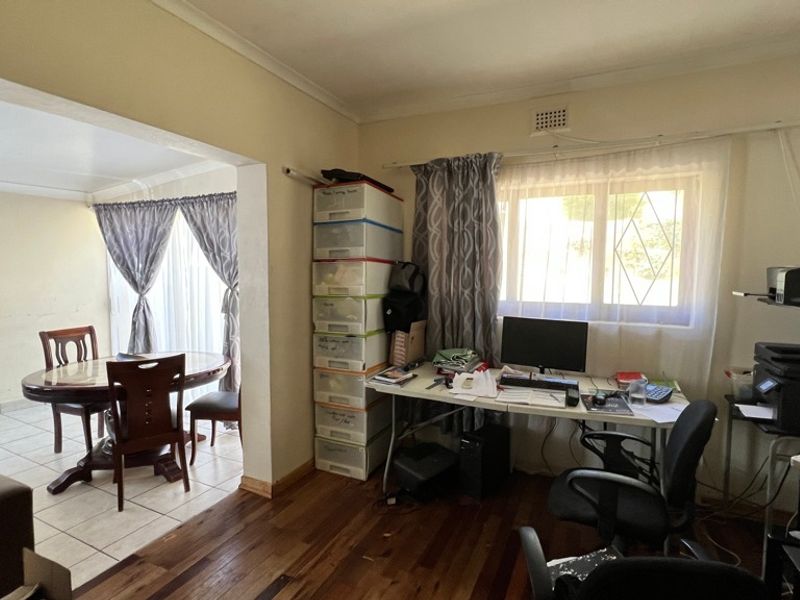 Open-plan living area featuring a combination of hardwood and tiled flooring, with a connected dining space and natural light through a security-fitted window.