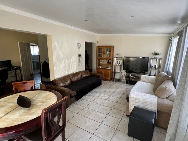 An open-plan living and dining area featuring neutral tiled flooring, recessed ceiling lighting, and coving throughout the space.