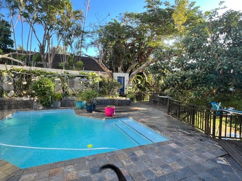 Outdoor pool area featuring stone tile paving, timber decking, and a timber balustrade, surrounded by established garden landscaping.