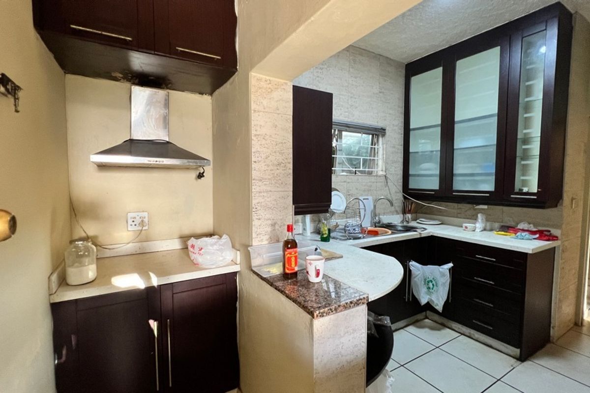 A functional kitchen featuring dark wood cabinetry, stone countertops, a stainless steel extractor fan, and tiled flooring, with some visible wear on the ceiling.