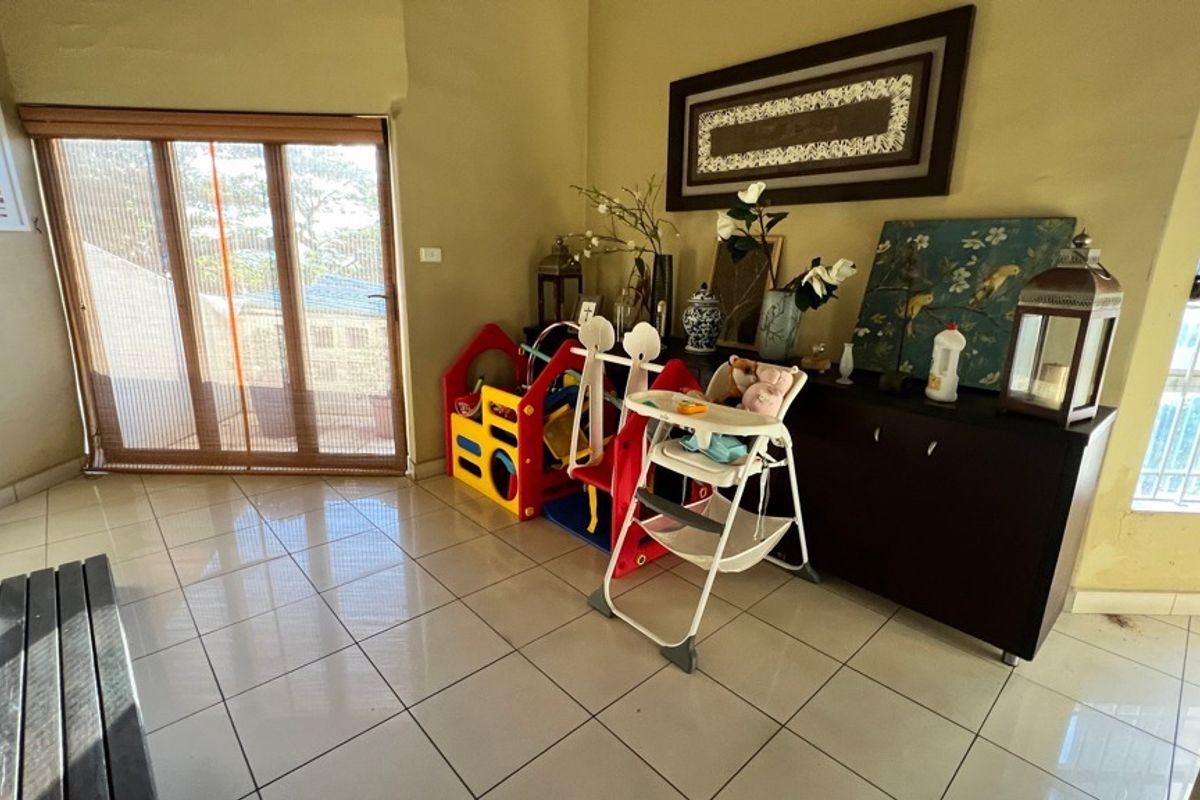 A living area featuring neutral tiled flooring, a sliding glass door leading to an outdoor space, and windows with security bars.