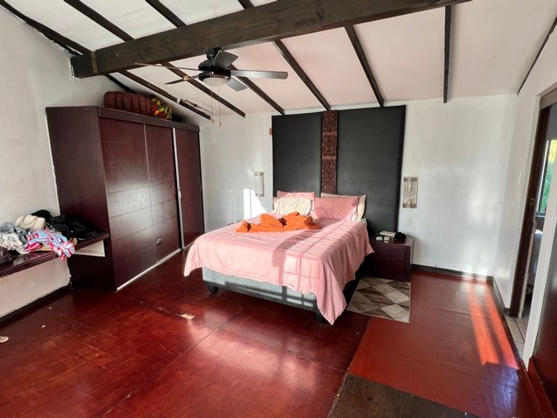 Spacious bedroom featuring exposed timber ceiling beams, a ceiling fan, and extensive built-in cabinetry with a matching integrated headboard.
