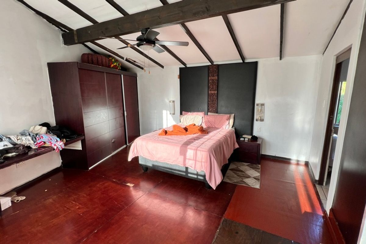 Spacious bedroom featuring exposed timber ceiling beams, a ceiling fan, and extensive built-in cabinetry with a matching integrated headboard.