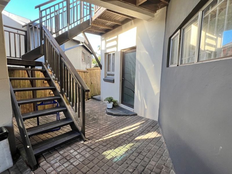 A paved rear courtyard area featuring an external staircase providing access to the upper level and secure timber fencing.