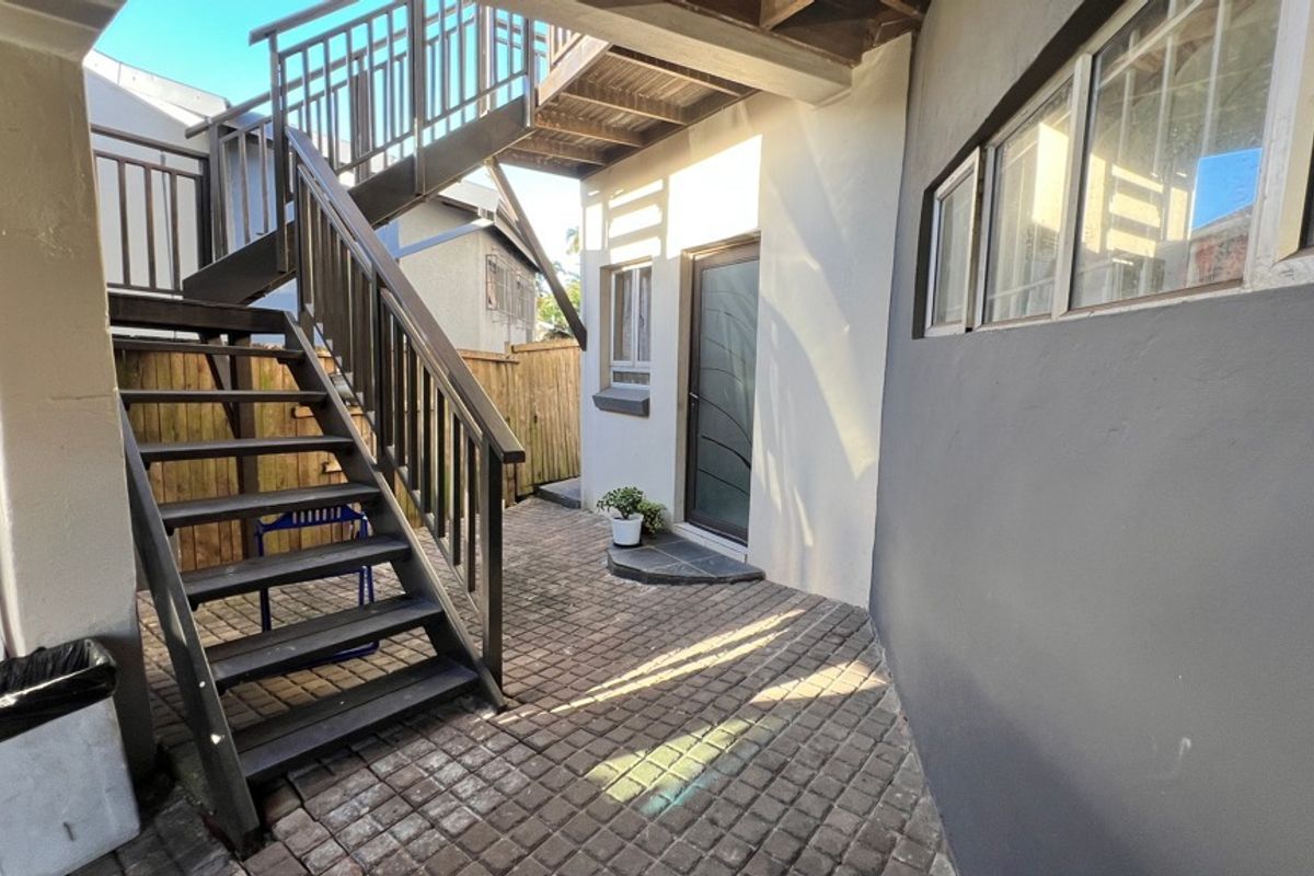 A paved rear courtyard area featuring an external staircase providing access to the upper level and secure timber fencing.