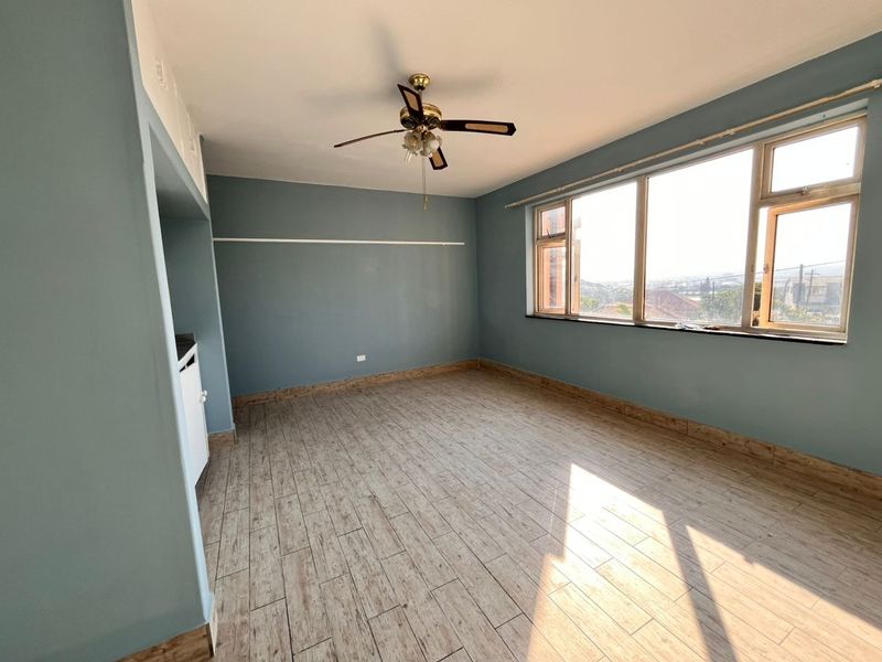 An empty living room featuring wood-look tiled flooring, a ceiling fan, and a large window providing natural light and an elevated view.