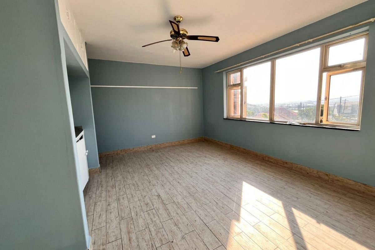 An empty living room featuring wood-look tiled flooring, a ceiling fan, and a large window providing natural light and an elevated view.