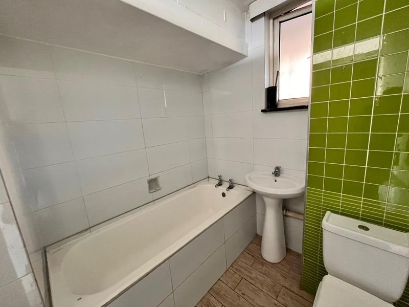 A functional bathroom featuring a bathtub, pedestal sink, toilet, and a combination of white and green wall tiling.