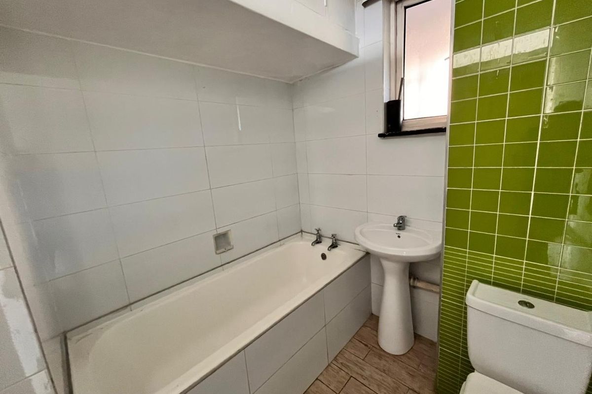 A functional bathroom featuring a bathtub, pedestal sink, toilet, and a combination of white and green wall tiling.