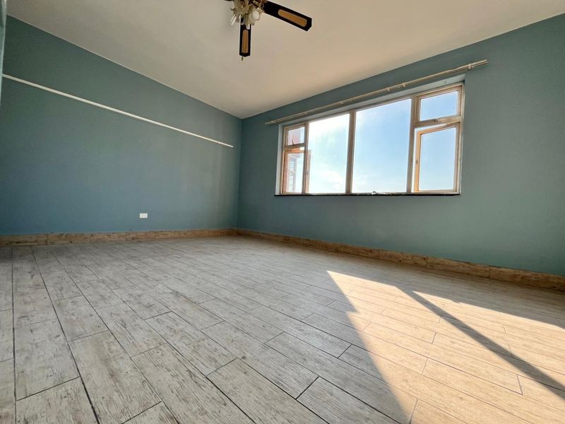 A spacious, empty bedroom featuring light wood-look tiled flooring, blue painted walls, and a ceiling fan, offering a bright and versatile living space.