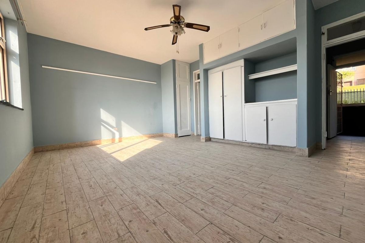 Spacious bedroom featuring light wood-look tiled flooring, built-in storage cupboards, and a ceiling fan, offering a clean and neutral canvas.