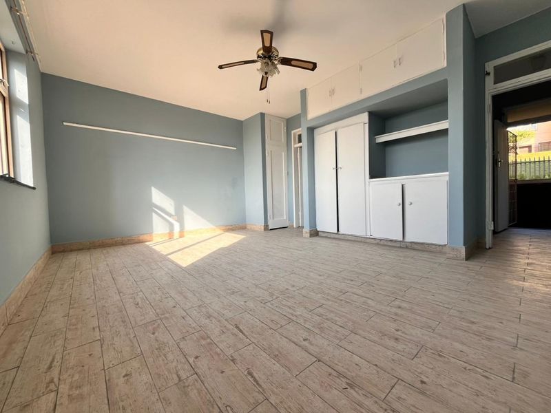 Spacious bedroom featuring light wood-look tiled flooring, built-in storage cupboards, and a ceiling fan, offering a clean and neutral canvas.