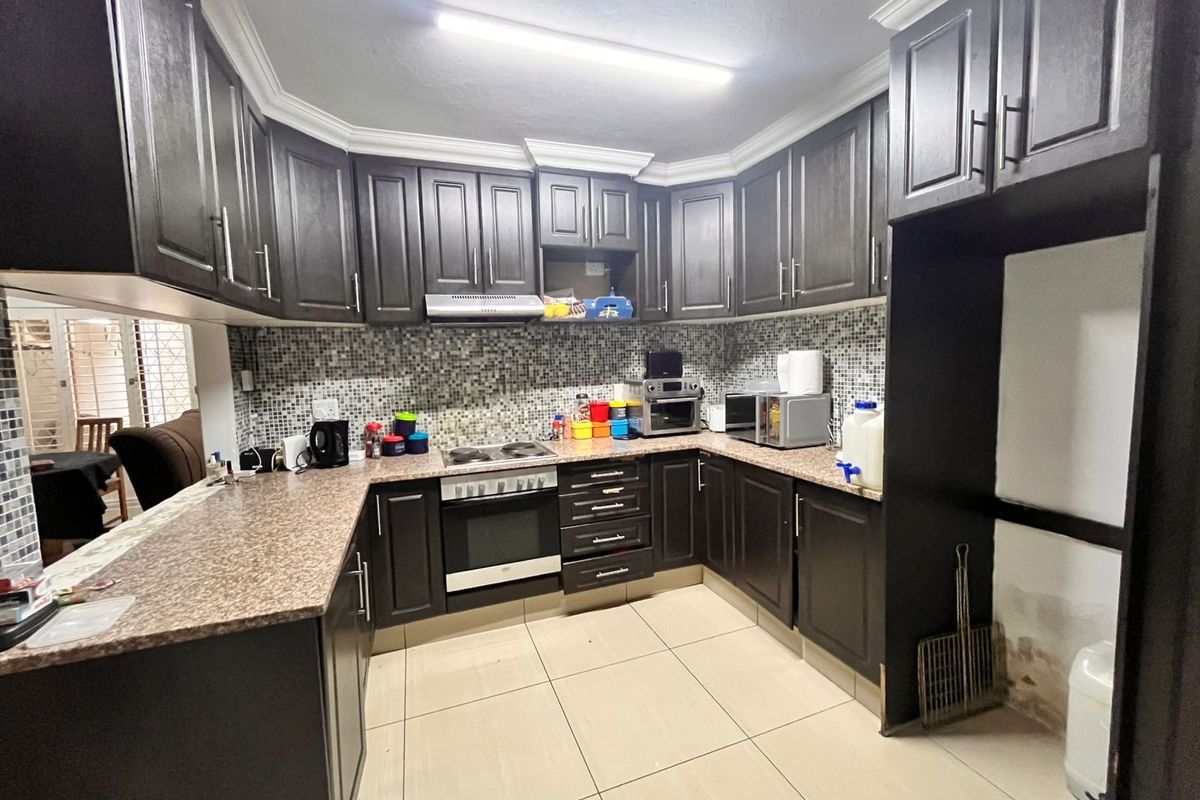 A functional kitchen featuring dark wood cabinetry, granite countertops, mosaic tile backsplash, and built-in cooking appliances with ceramic floor tiles.