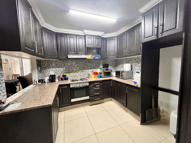A functional kitchen featuring dark wood cabinetry, granite countertops, mosaic tile backsplash, and built-in cooking appliances with ceramic floor tiles.