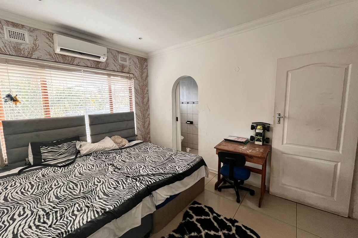 Bedroom featuring tiled flooring, a split-system air conditioner, and an arched doorway leading to an en-suite bathroom.