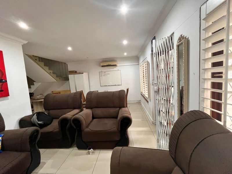 Open-plan living area featuring tiled flooring, recessed downlights, a split-system air conditioner, and a staircase leading to the upper level.
