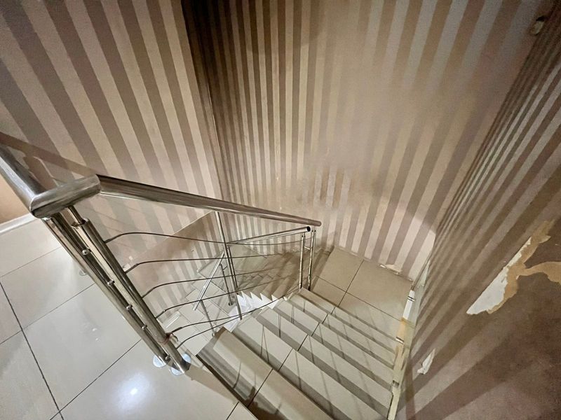 A staircase area featuring tiled flooring, a stainless steel balustrade, and striped wallpaper showing signs of wear and peeling.