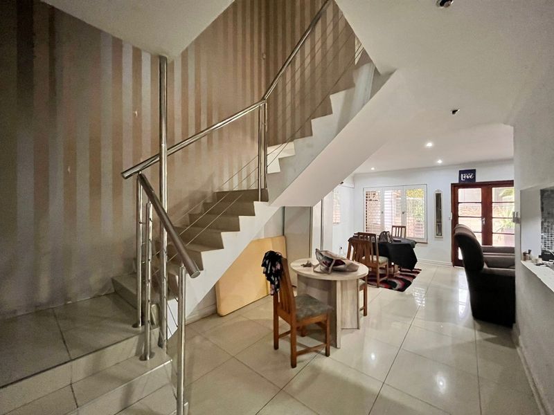 Open plan living area featuring tiled flooring, recessed lighting, and a modern stainless steel staircase railing leading to the upper level.