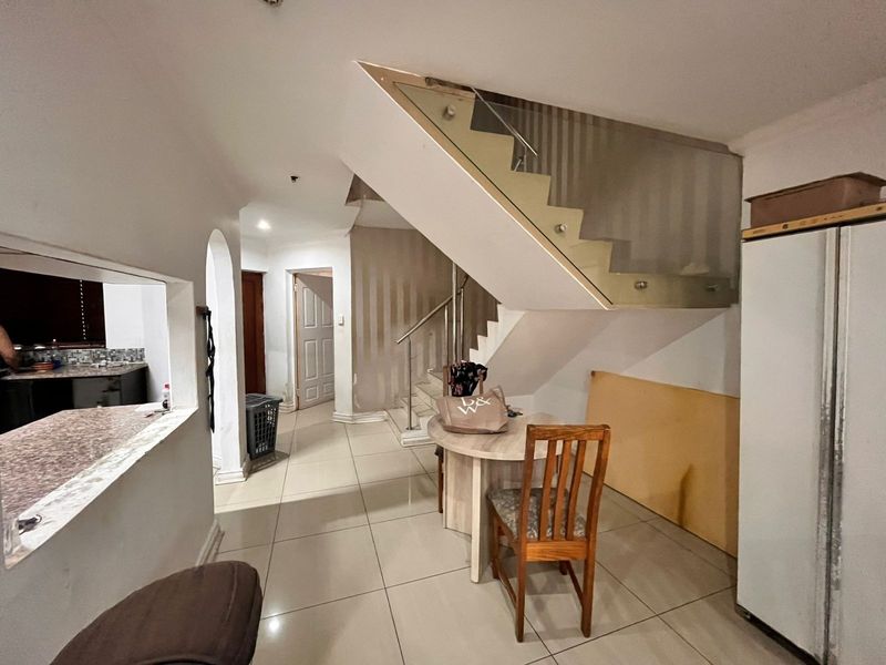 Open plan living area featuring a modern glass balustrade staircase, tiled flooring, and a convenient pass-through window connecting to the kitchen space.