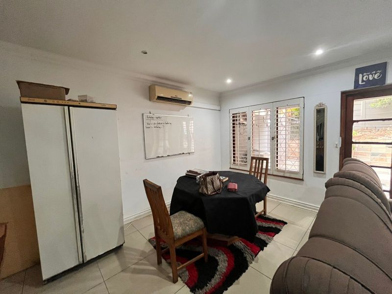 A living area featuring tiled flooring, recessed downlighting, and security shutters on the windows, equipped with a wall-mounted split-system air conditioner.