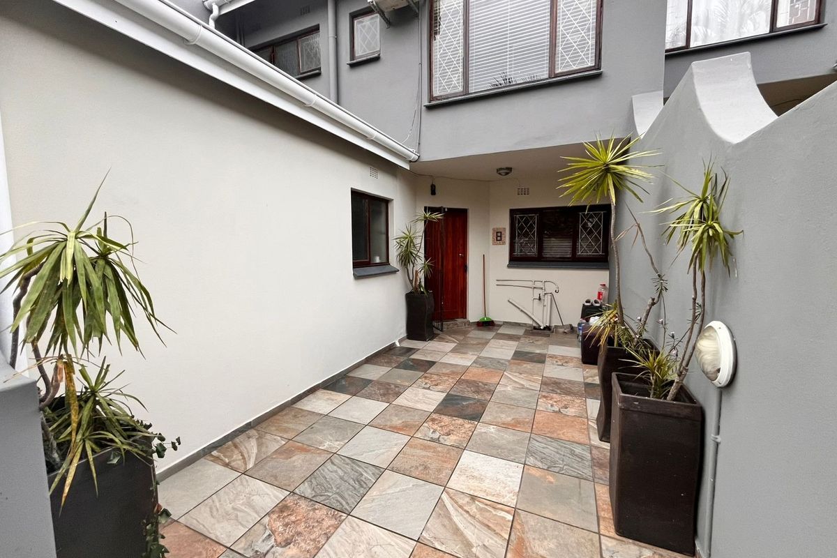 A paved rear courtyard area featuring tiled flooring, external wall lighting, and security bars on the windows of the townhouse.