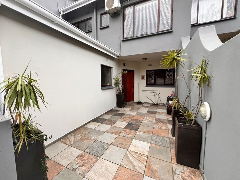 A paved rear courtyard area featuring tiled flooring, external wall lighting, and security bars on the windows of the townhouse.