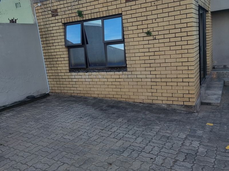 Rear exterior view of a face brick structure featuring aluminium windows and a paved courtyard area requiring maintenance.