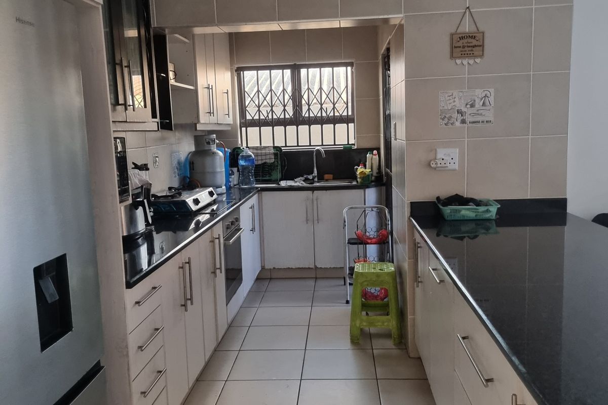 A functional kitchen featuring granite countertops, tiled flooring, built-in oven, and hob, with a practical layout and ample cabinetry for storage.