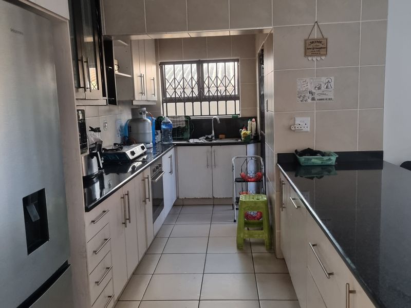 A functional kitchen featuring granite countertops, tiled flooring, built-in oven, and hob, with a practical layout and ample cabinetry for storage.